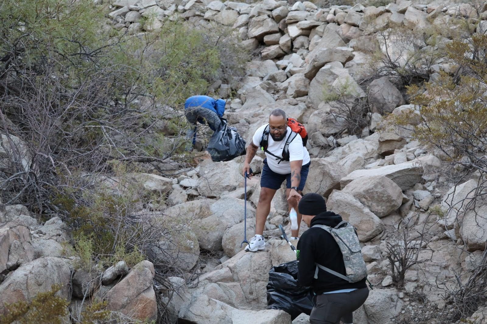 Volunteers with grabbers filling trash bags on a rocky hillside
