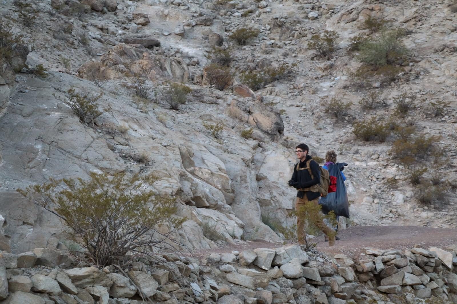 Two volunteers carrying trash bags along a desert mountain trail