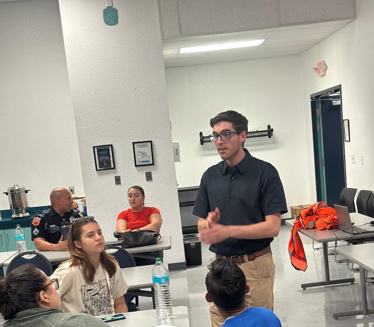 An NMOI instructor speaking with volunteers and a police officer seated at tables