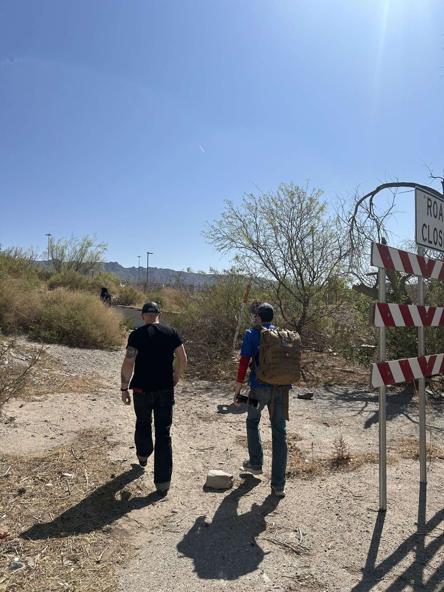 Two outreach volunteers, one carrying a medical backpack, walking a dirt trail