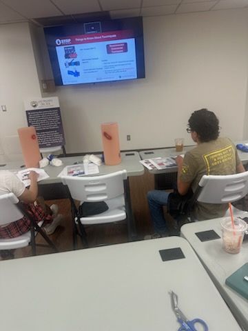 A trainee seated before a practice limb and a slide on tourniquets